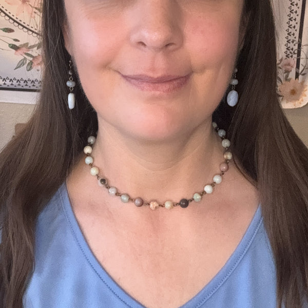 Person wearing an amazonite beaded necklace with earrings, against a neutral background