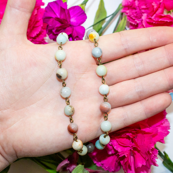 Hand holding an amazonite beaded necklace with pink flowers in the background