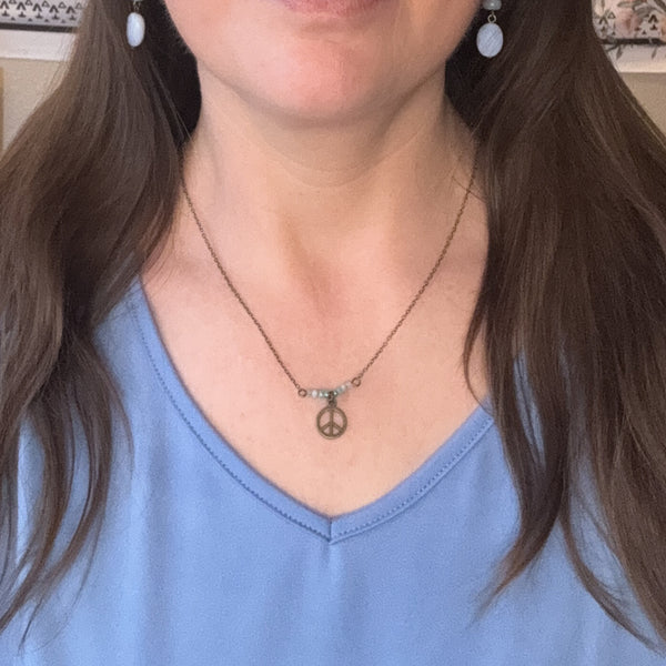 Person wearing a blue top and necklace with a peace sign pendant.