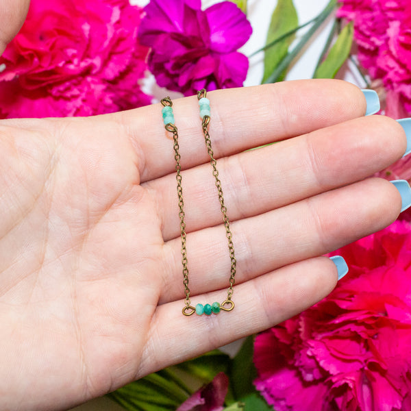 Gold chain necklace with amazonite beads held in a hand against pink flowers