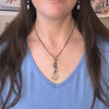 Person wearing a blue top and a necklace with a peace sign pendant.