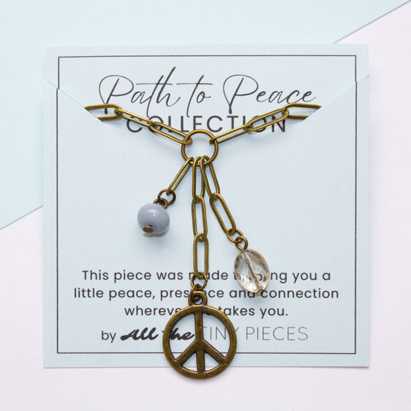 Brass chain necklace with peace symbol pendant on a 'Path to Peace' card