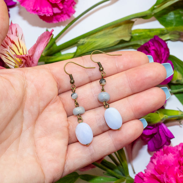 Hand holding a pair of blue lace agate earrings with flowers in the background