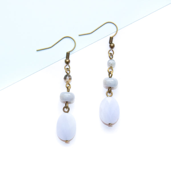 Pair of earrings with blue lace agate beads and brass hooks on a light blue background