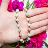 Hand holding an amazonite beaded necklace with pink flowers in the background