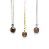 Three necklaces with smoky quartz pendant stones on gold, silver, and brass chains against a white background.