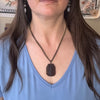 Person wearing a smoky quartz necklace with a blue top in an indoor setting
