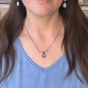 Person wearing a blue top and necklace with a peace sign pendant.