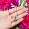 Hand holding a necklace with a peace sign pendant against a background of pink flowers