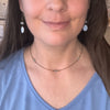 Close-up of a person wearing a necklace and earrings with a neutral background