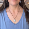 Close-up of a person wearing a necklace with an oval amazonite pendant on a blue top.