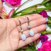 Hand holding a pair of blue lace agate earrings with flowers in the background